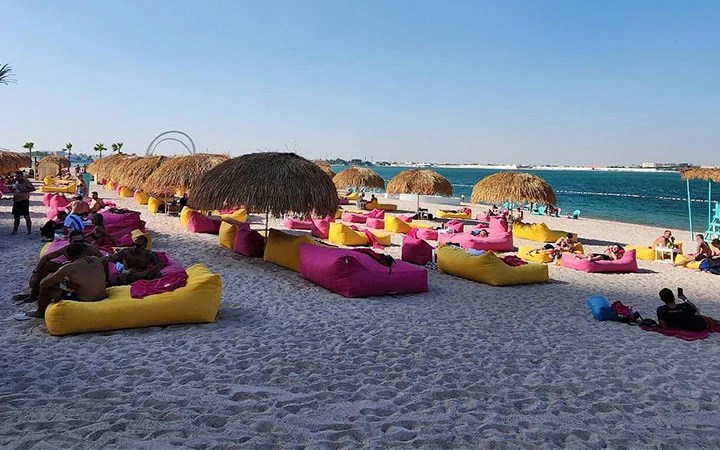 Colorful loungers and palm shades on the sandy beach at Doha Beach Club