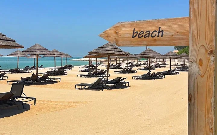 Wooden beach sign on sandy shore in Doha
