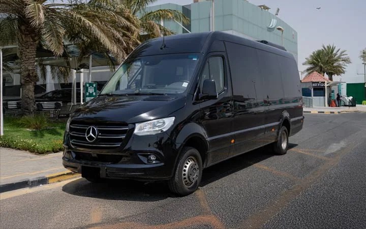 A black Mercedes Sprinter VIP Bus is parked on a city street in Doha, near palm trees and modern buildings under a clear sky.