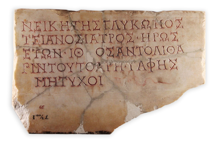 A rectangular stone plaque inscribed with five lines of Greek text. The beige plaque is significantly cracked and chipped.