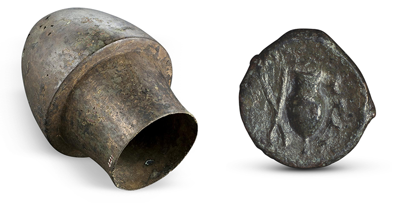 Imperfect circle composed of a dark, greenish-brown metal. Raised, indistinct shapes decorate the center. 