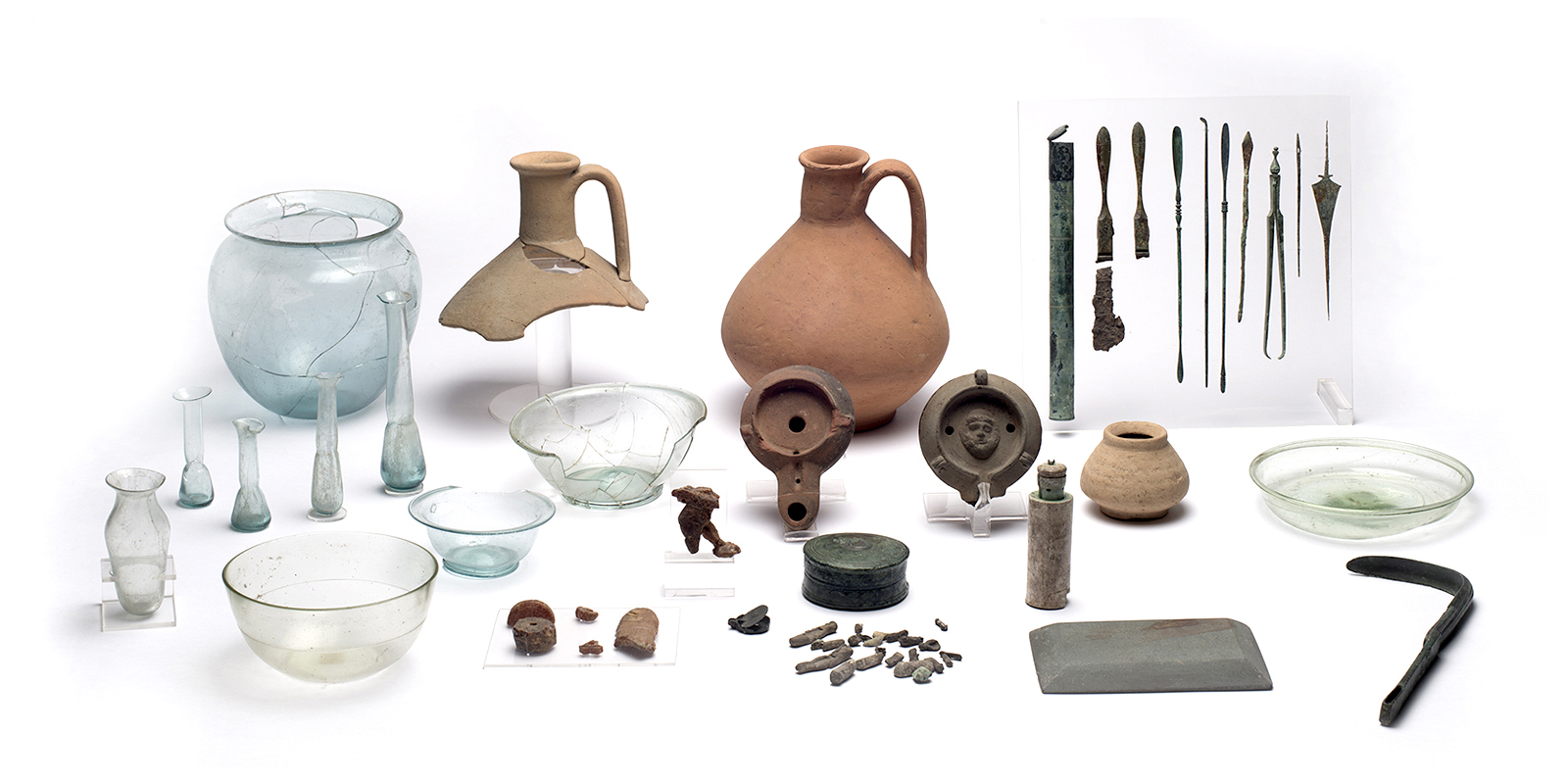 A collection of light blue bowls and vials, orange vases, one broken, two lamps, and greenish-brown pencil-like tools. 