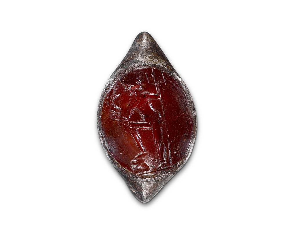 A circular object made of a translucent red material set in silver. The red center has been carved with a male figure holding a trident. 