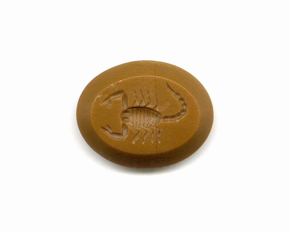 Oblong, yellowish-orange stone with a beveled edge. A scorpion is carved into the center. 