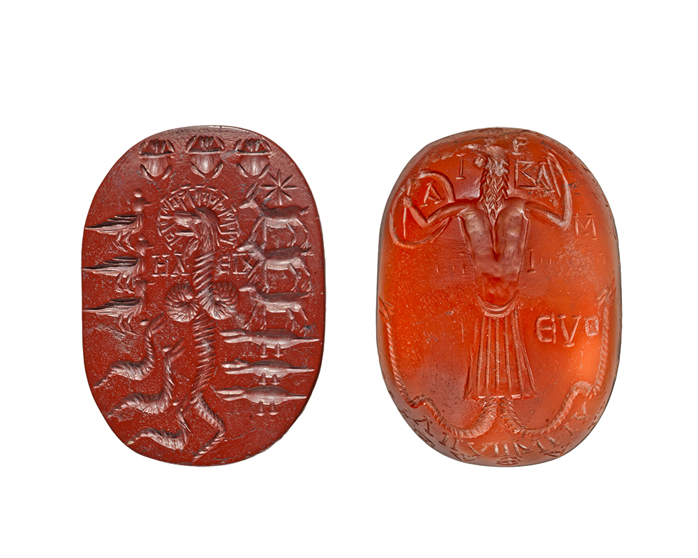 The front and back of a red, vertically oriented, oval stone. On the left, the stone is inscribed with crocodiles, goats, birds, scarab beetles, and dragons around a snake-like monster. On the right, the stone displays a lion-headed creature with some text symbols.
