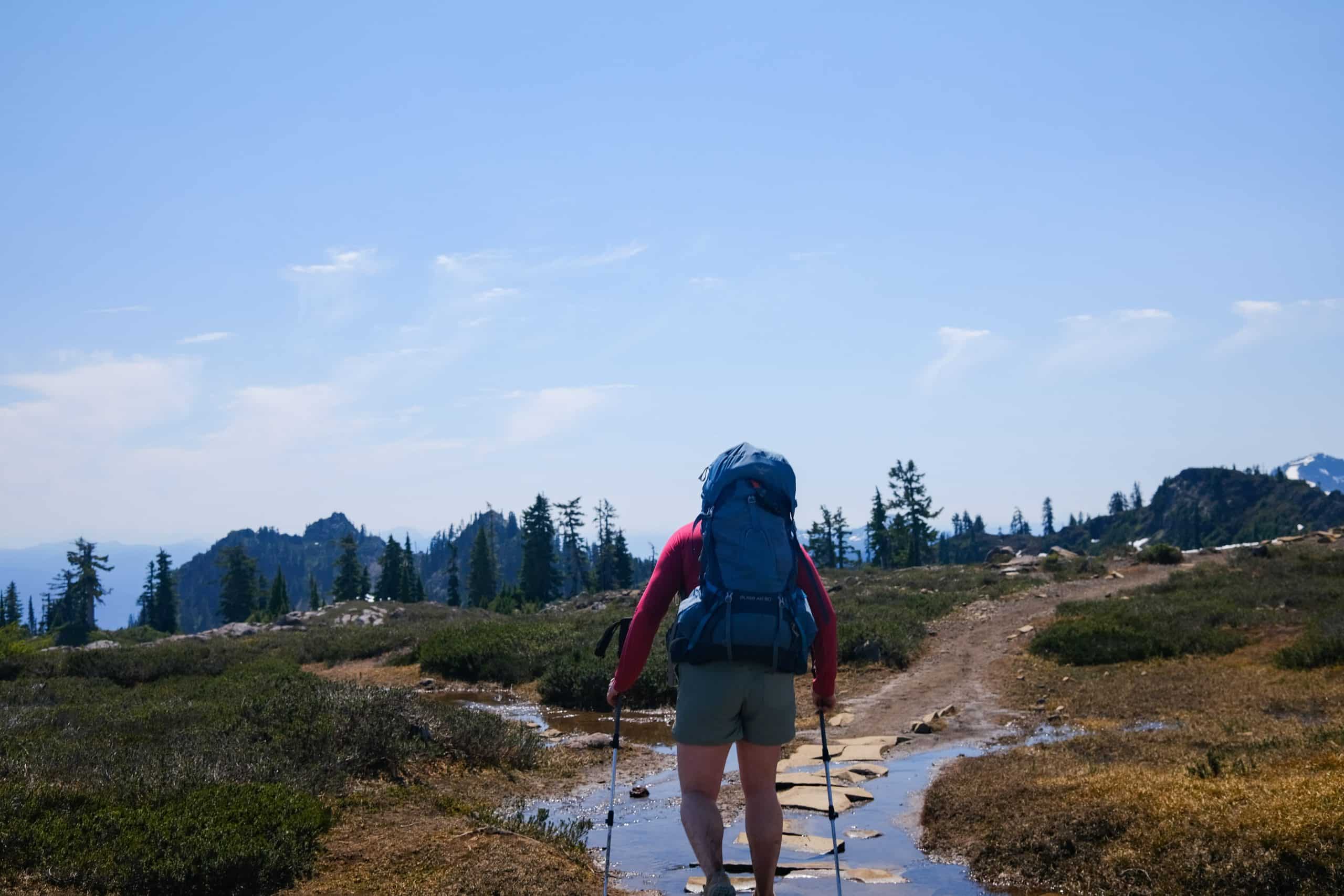 women with large blue backpack walking on a watery trail