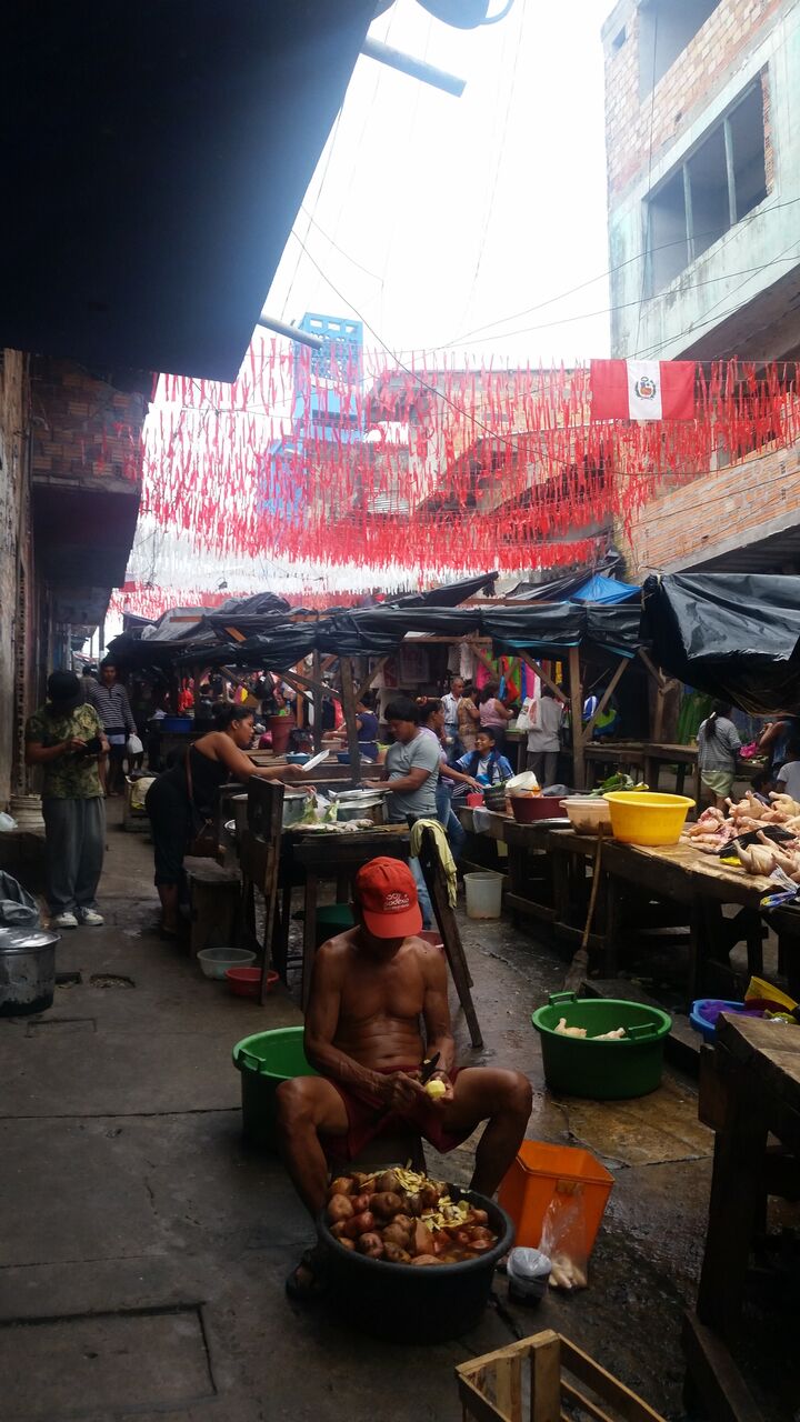 Shirtless man in red hat peeling vegetable in Belen market Iquitos.