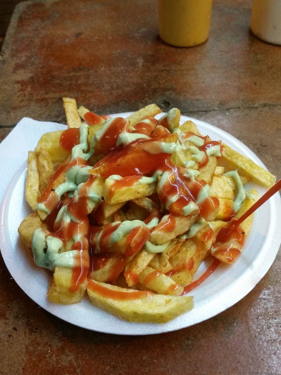 Plate of french fries with ketchup and green sauce.