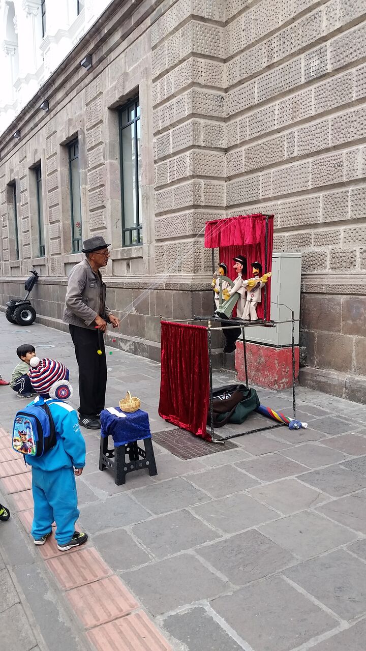 Man playing street puppets with a red velvet curtain and a child in blue watching.