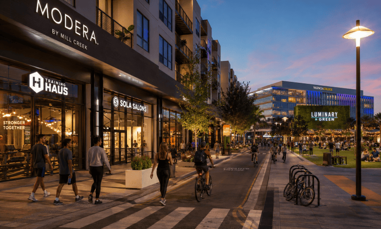 Street-level evening view of Modera Creative Village, active retail storefronts, pedestrians and cyclists beside Luminary Green in Downtown Orlando.