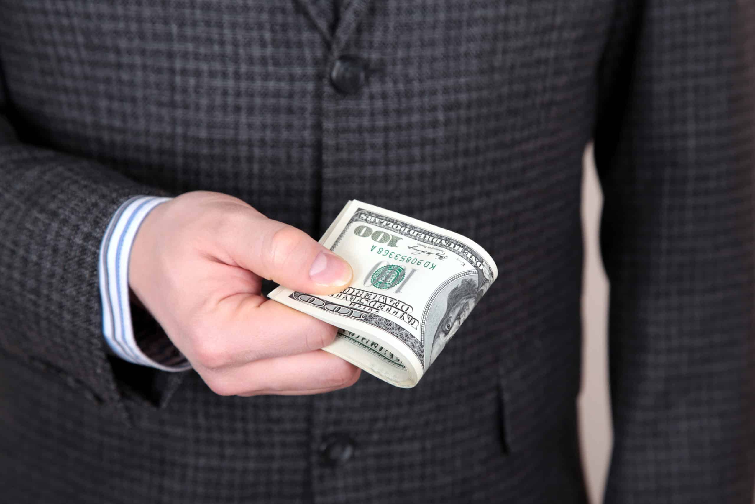 persona con traje teniendo un fajo de billetes de dolares
