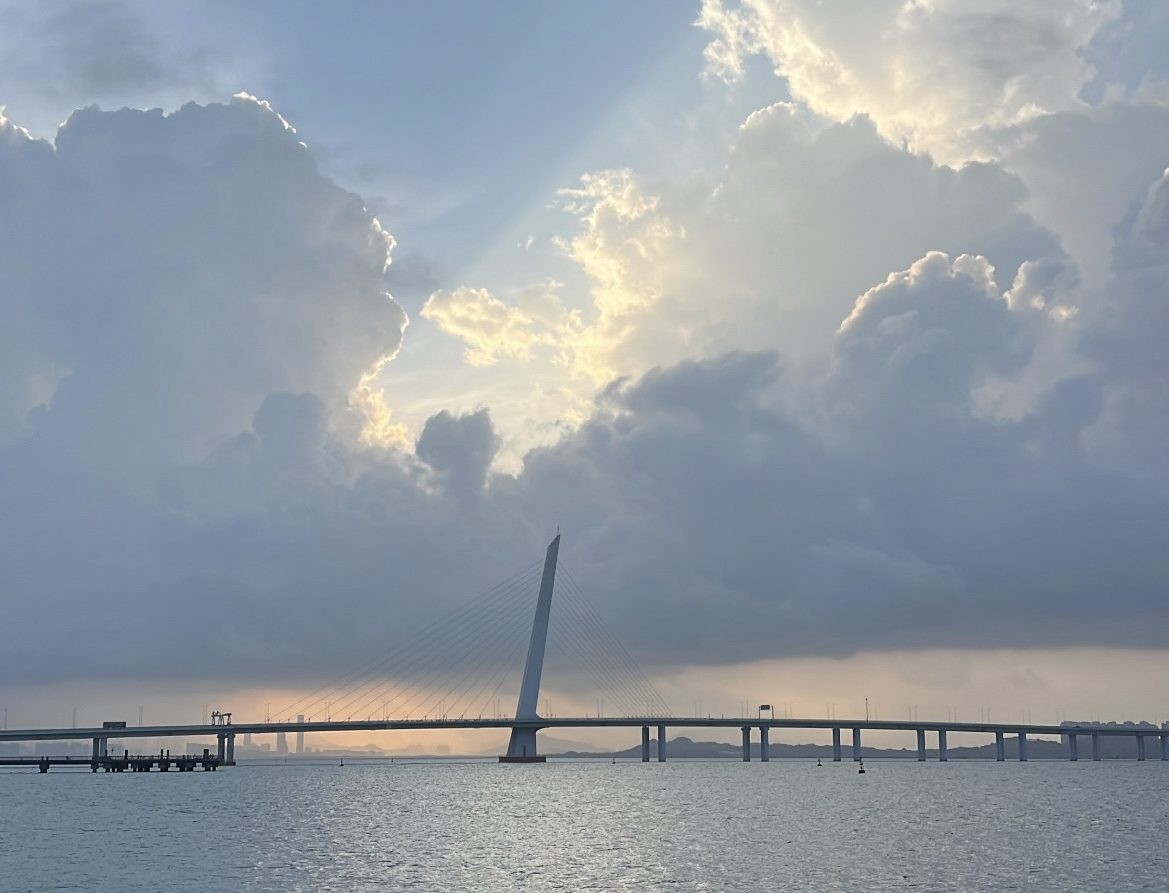 Scenic view of a bridge over the water, with dramatic clouds and sunlight peeking through the sky.