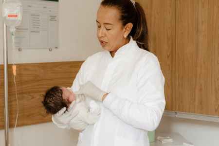 a woman in white coat holding a baby in a hospital bed