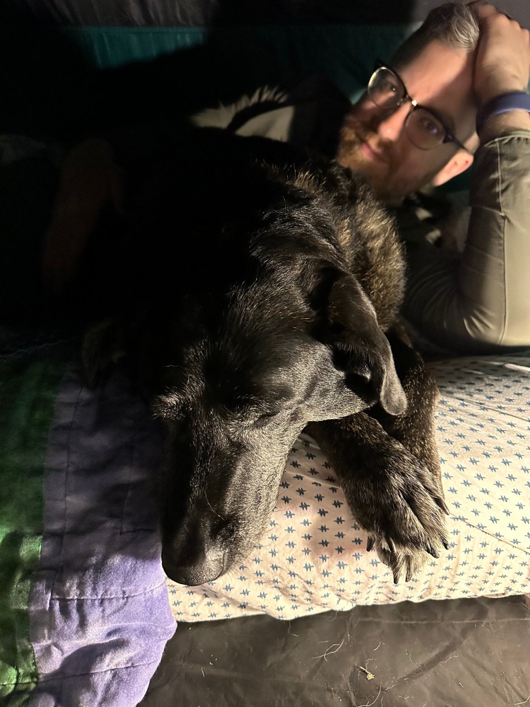 picture of Carolina, our black lab, with paws crossed, cuddled up with Jonathan