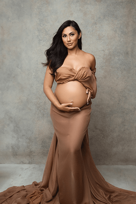 Maternity portrait in a draped brown gown against a textured backdrop.