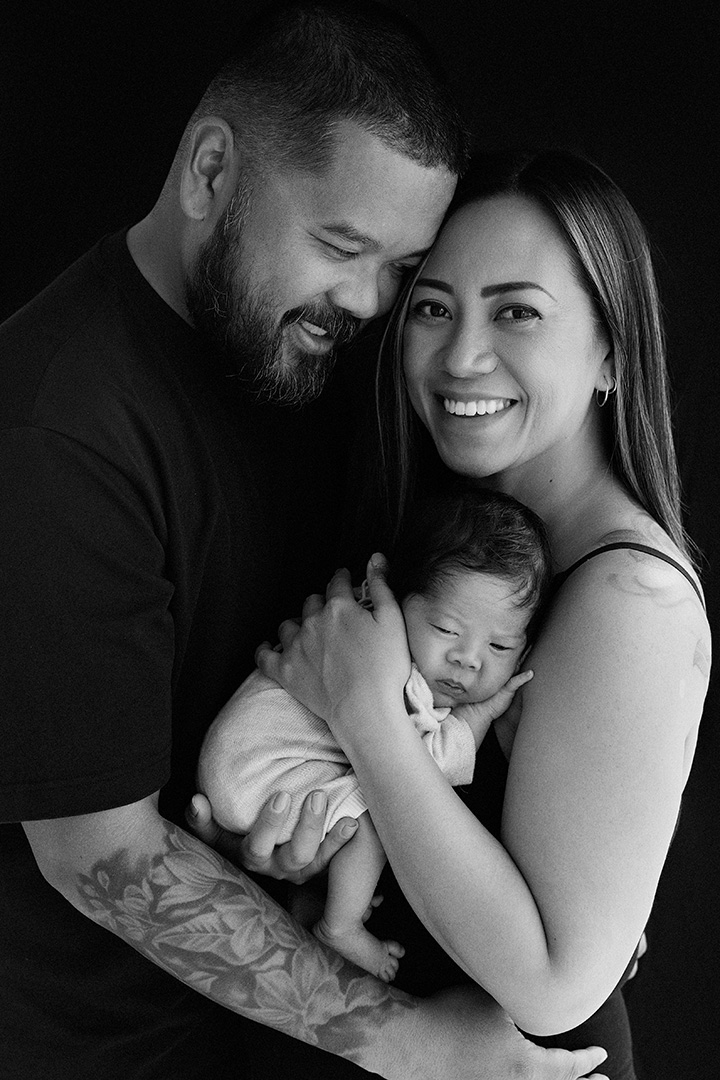Black-and-white portrait of parents holding their sleeping newborn.
