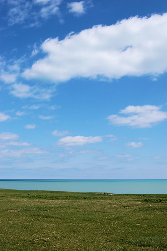 puffy clouds in sky over lake that is two blues and green grass shore