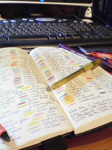 Computer keyboard in background with open journal page showing various color swatches of ink with pen names written beside them gold pen on top of journal