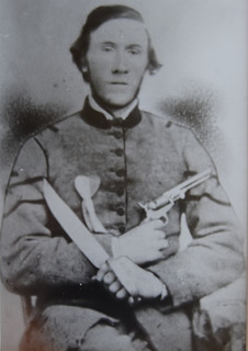 posing in Confederate uniform with saber and gun.  There is a heart shaped medal on his chest.