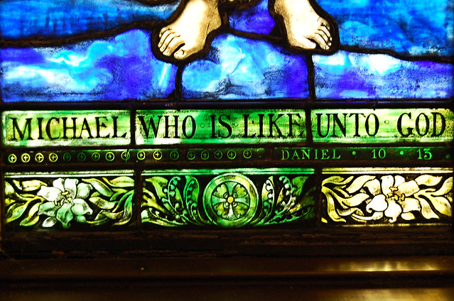 Michael  who is like unto God written under the feet with lily motif below that