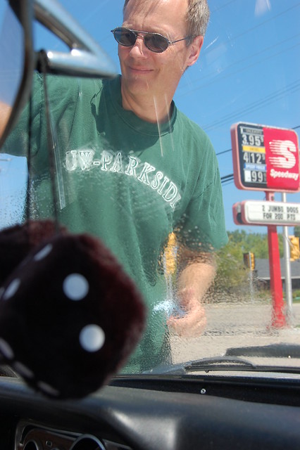 photo has fuzzy dice in foreground, the windshield is partially clean the rest is soapy as mike cleans the windshield.  