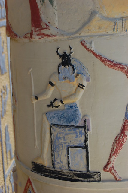 a dung beetle faced deity sits on a throne enshrined as Pharaoh the image has been partially painted