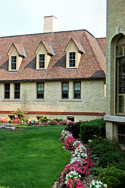 Chalk brick building with begonia in white and pink trimming a manicured green lawn.