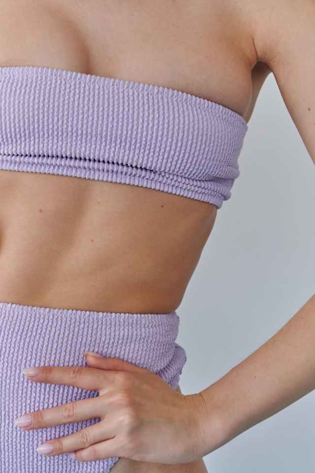Close-up of a woman's waist showcasing fitness and fashion in a lilac textured outfit.