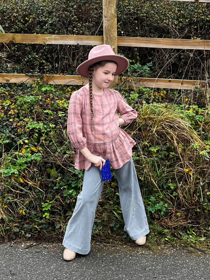 A small girl posing in flares and a western-style hat.