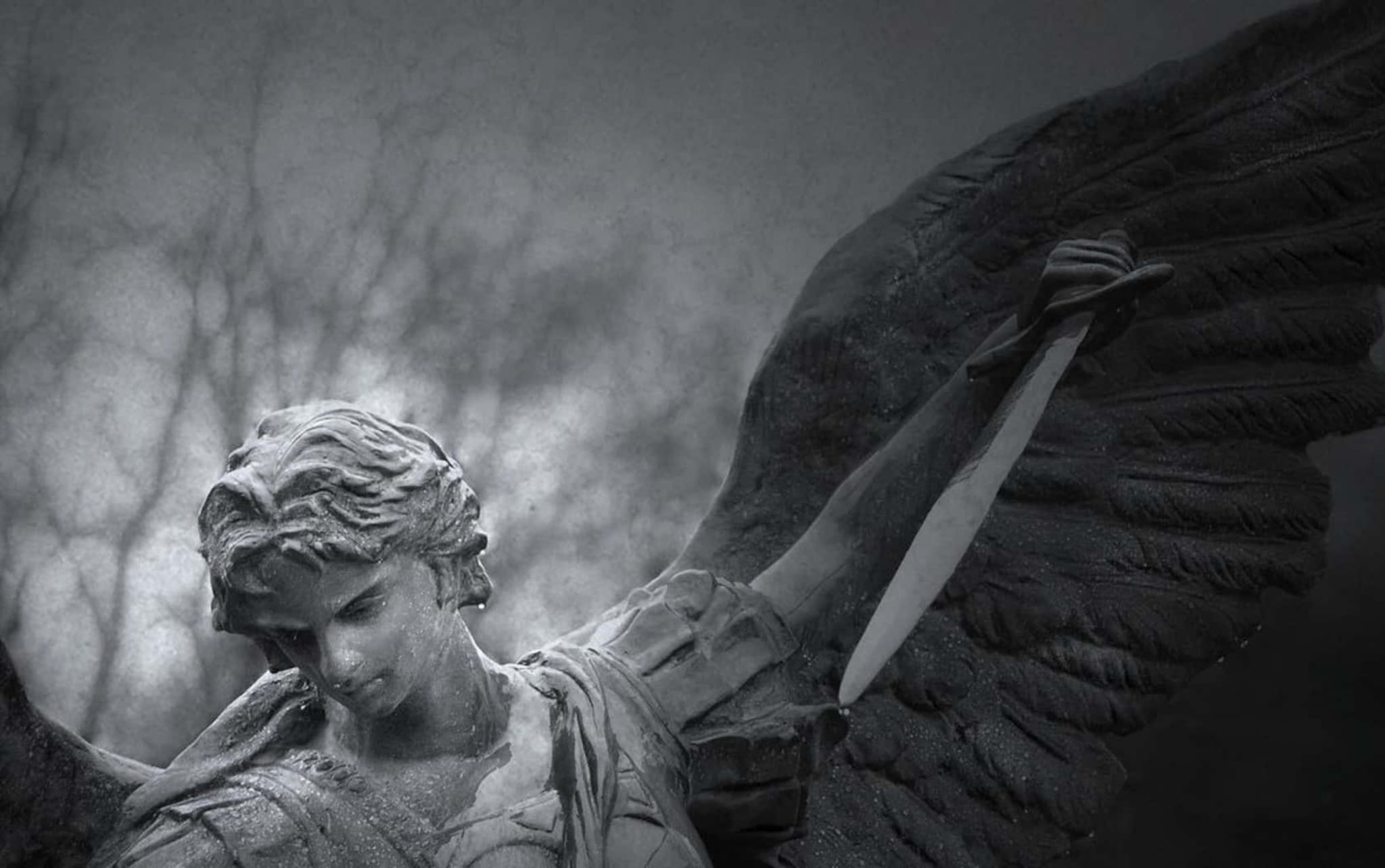 Dark, dramatic sculpture of a sorrowful angel with large wings, holding a sword, head bowed in grief amid misty trees.