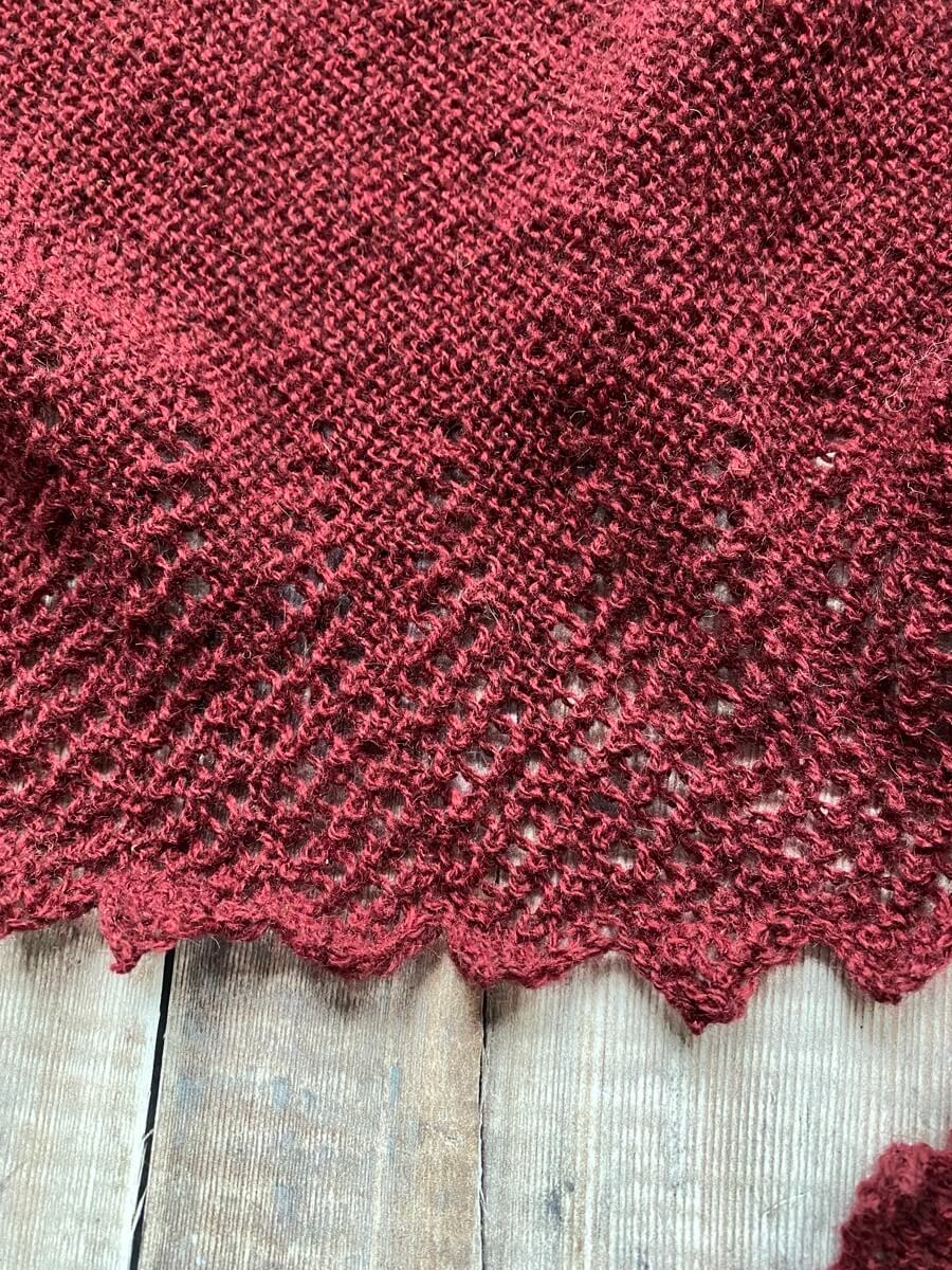 A closeup of a knitted hap's lace border before blocking. It looks unfinished and the stitches have no definition.