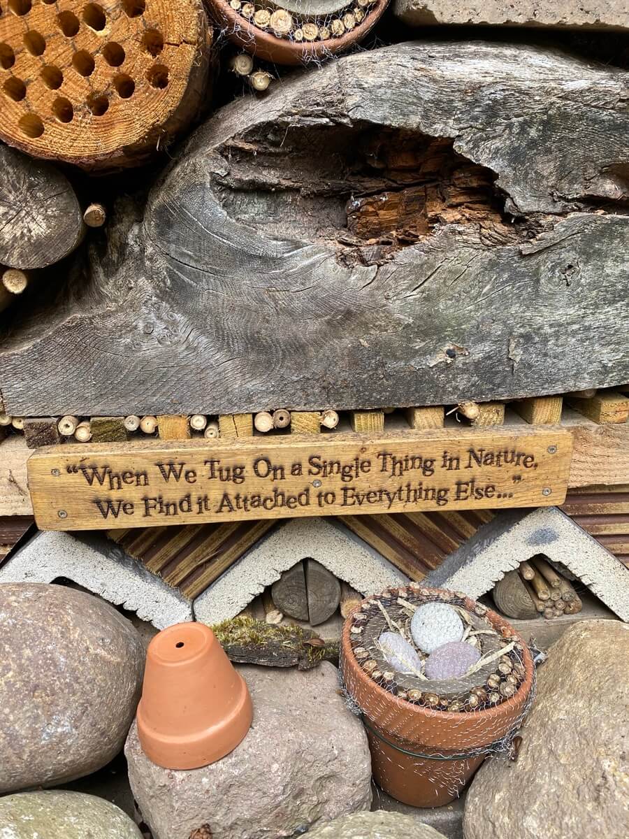 Bug hotel with saying on the bottom: "When we tug on a single thing in nature, we find it attached to everything else"