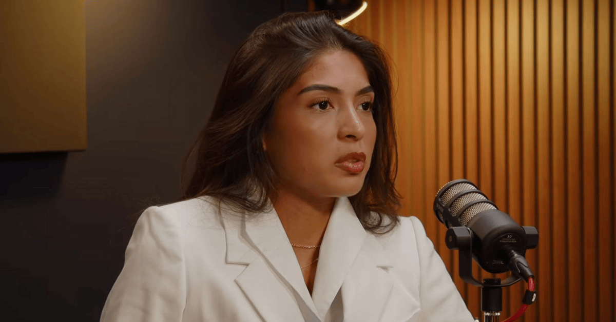 Woman in a white blazer speaking into a microphone during a podcast interview about a pageant controversy.