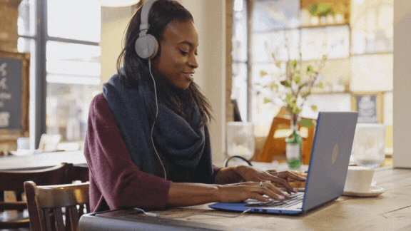 A woman transcribing a video over a laptop with headphones on