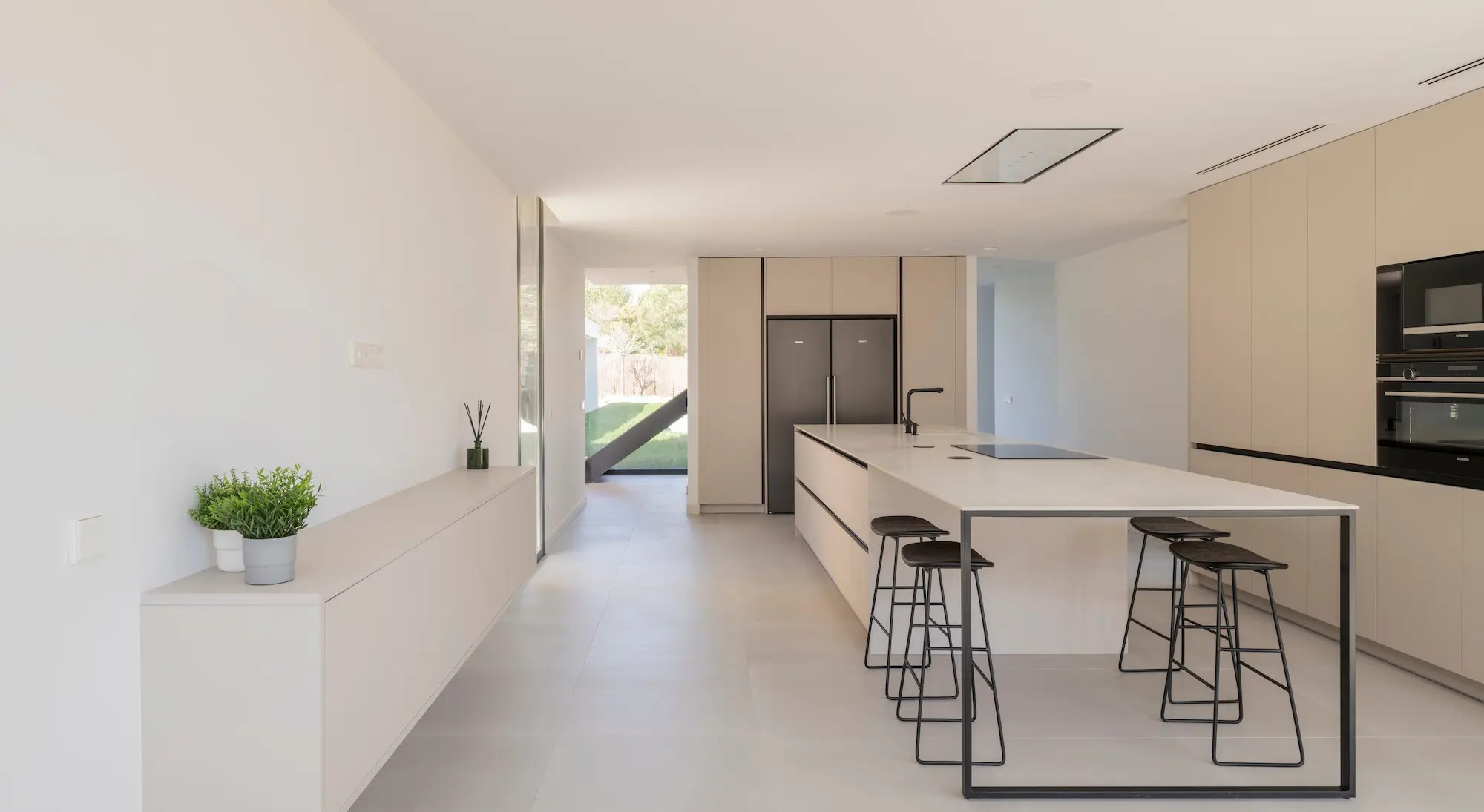Cocina minimalista de vivienda contemporánea en Villanueva de la Cañada, Madrid, con isla central, mobiliario beige y electrodomésticos integrados.