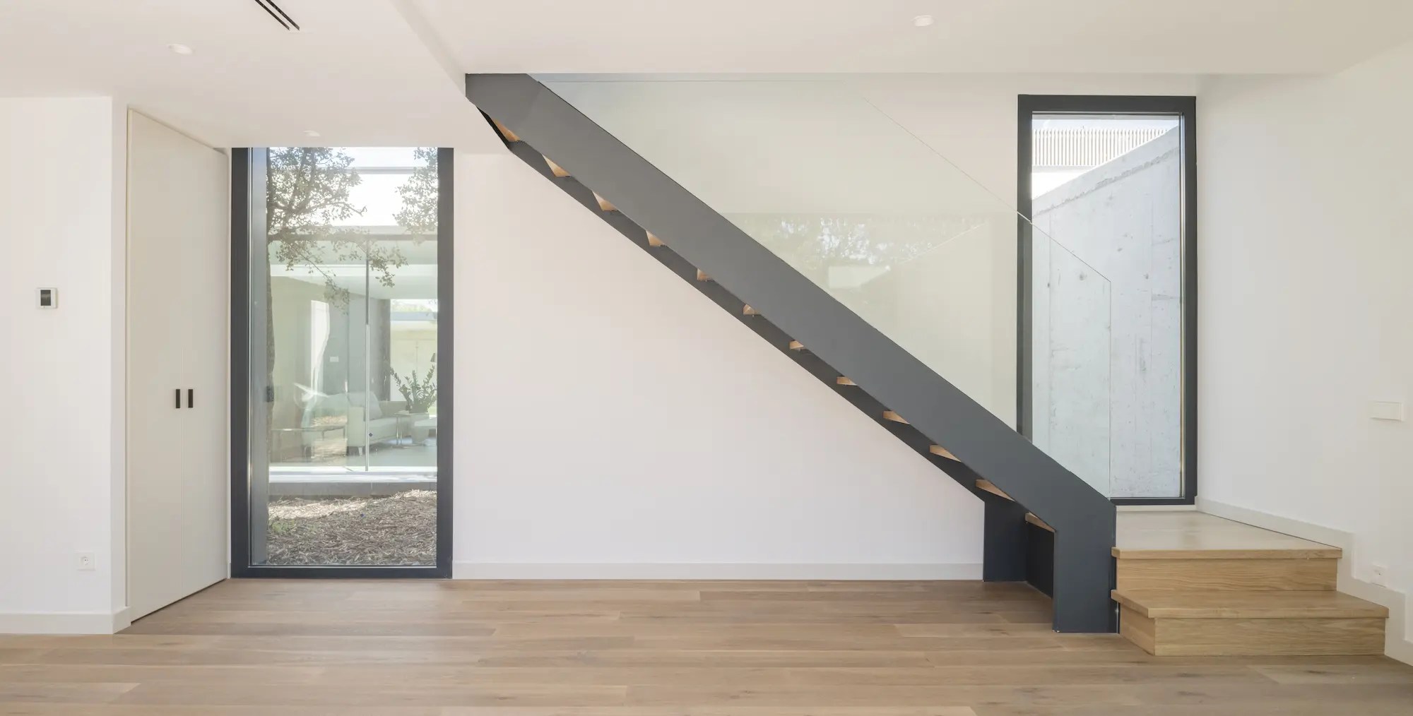 Interior de vivienda contemporánea en Villanueva de la Cañada, Madrid, con escalera de diseño en estructura metálica oscura y peldaños de madera.