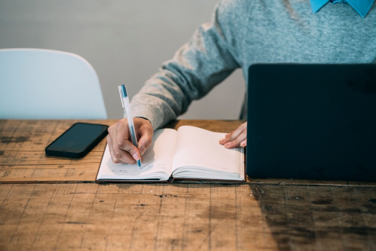Don't write alone. Person writing in a notebook and on a laptop.