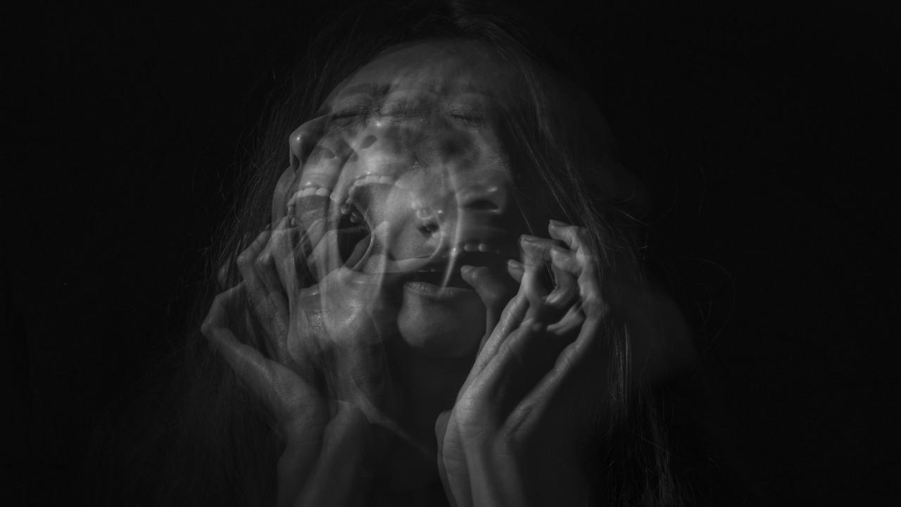 Em preto e branco, imagem distorcida com sobreposioções de uma mulher gritando e com as mãos no rosto.