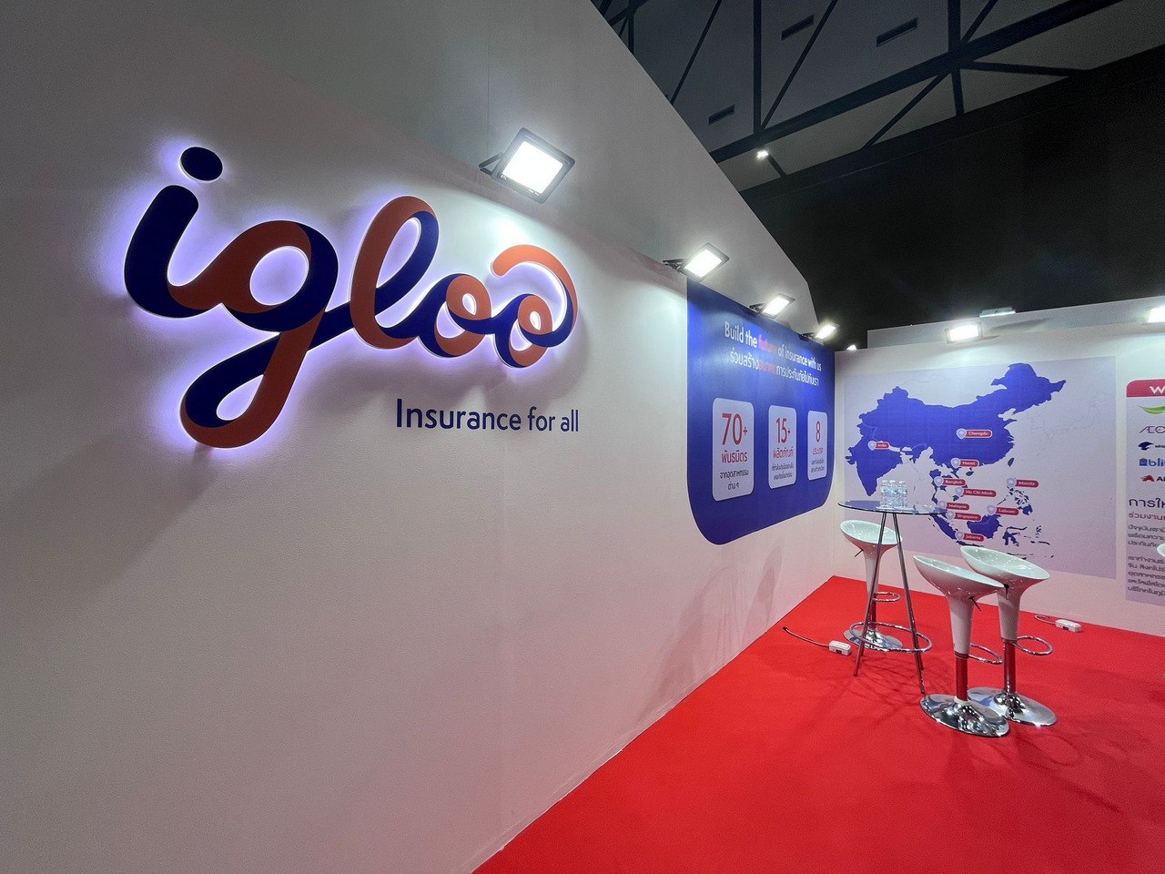 A trade show booth for Igloo, a digital insurtech company, featuring a brightly lit logo on a white wall with the tagline "Insurance for all.