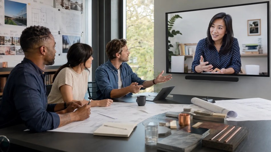 Engineers reviewing project drawings while collaborating with a marketing strategist through a large video conference screen