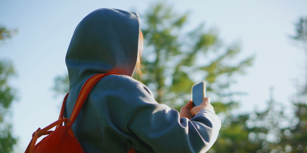 Person using phone deciding on Watch Duty alternatives with trees in the background