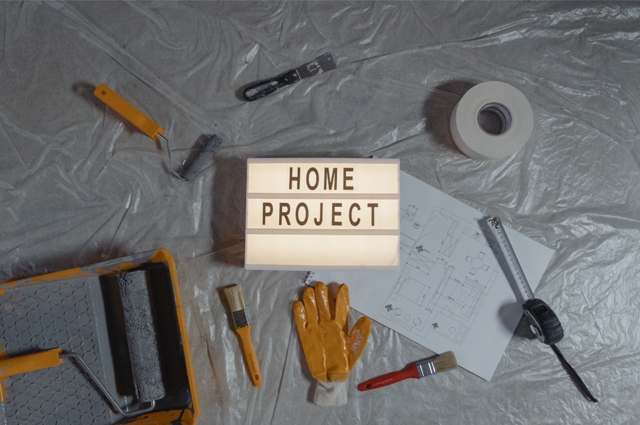 Home Project light box sign surrounded by a paint roller, brush, tape and gloves