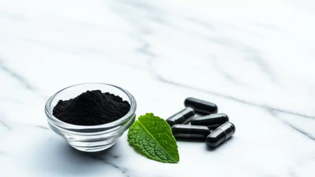 A bowl of activated charcoal powder next to several capsules on a clean marble surface, illustrating safe dosage information.