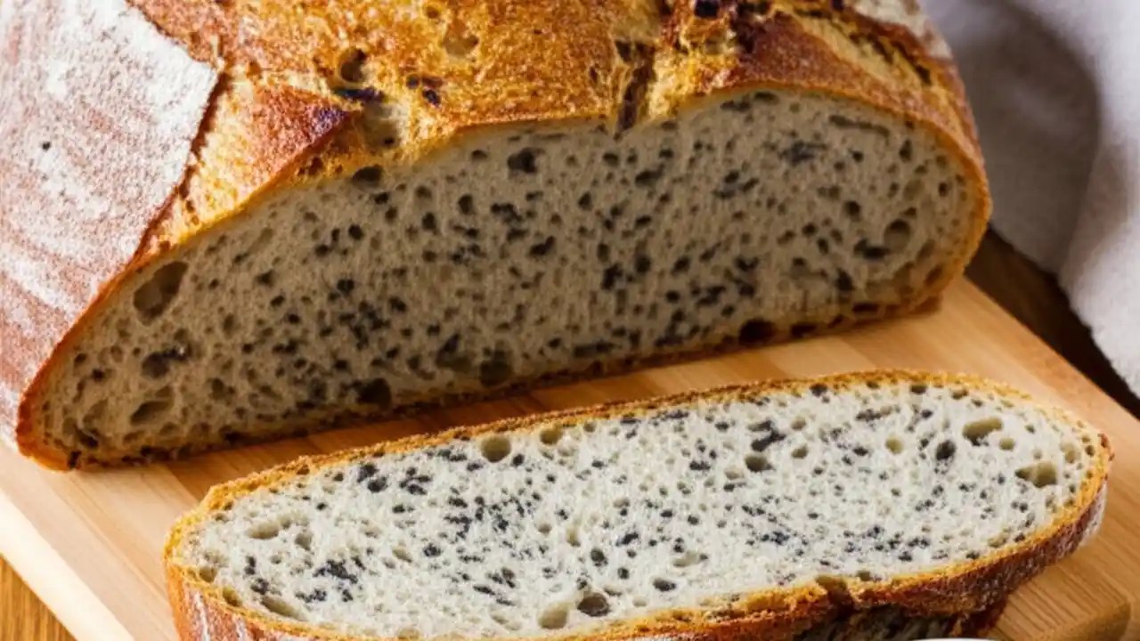 A freshly baked loaf of artisan bread sliced to show the soft crumb with visible ground flax seeds mixed into the dough.