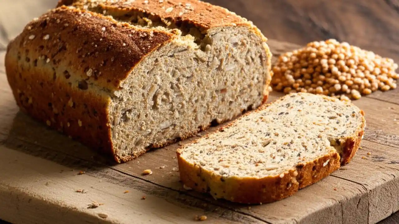 A sliced loaf of authentic Ezekiel bread on a wooden board, showing its dense, grainy texture.