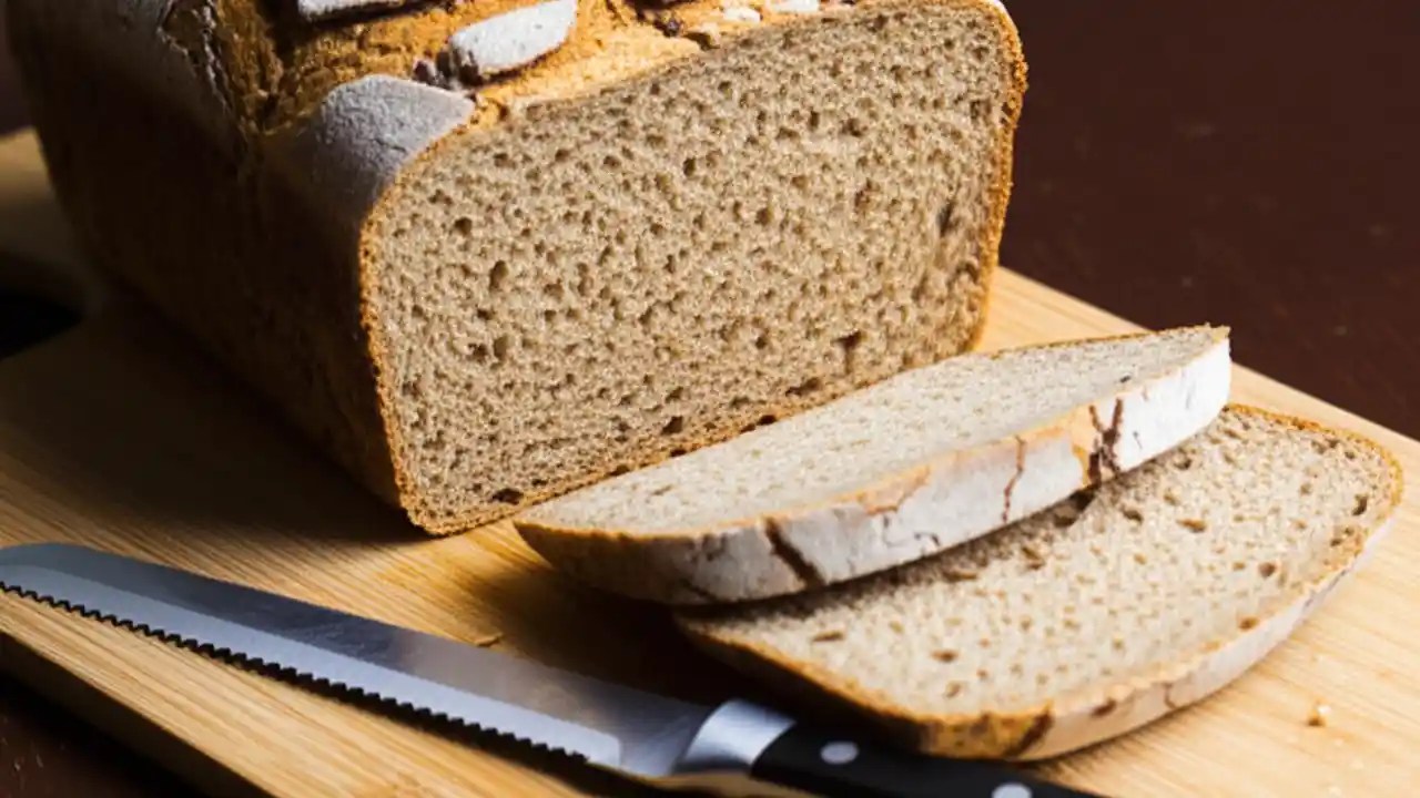 A finished loaf of homemade Jewish rye bread with a glossy, caraway-seed-covered crust, resting on a wooden board before being sliced.