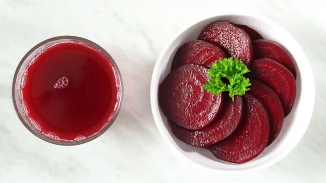 A glass of beetroot juice sits next to a bowl of sliced cooked beets on a clean marble surface, illustrating the choice between the two forms.