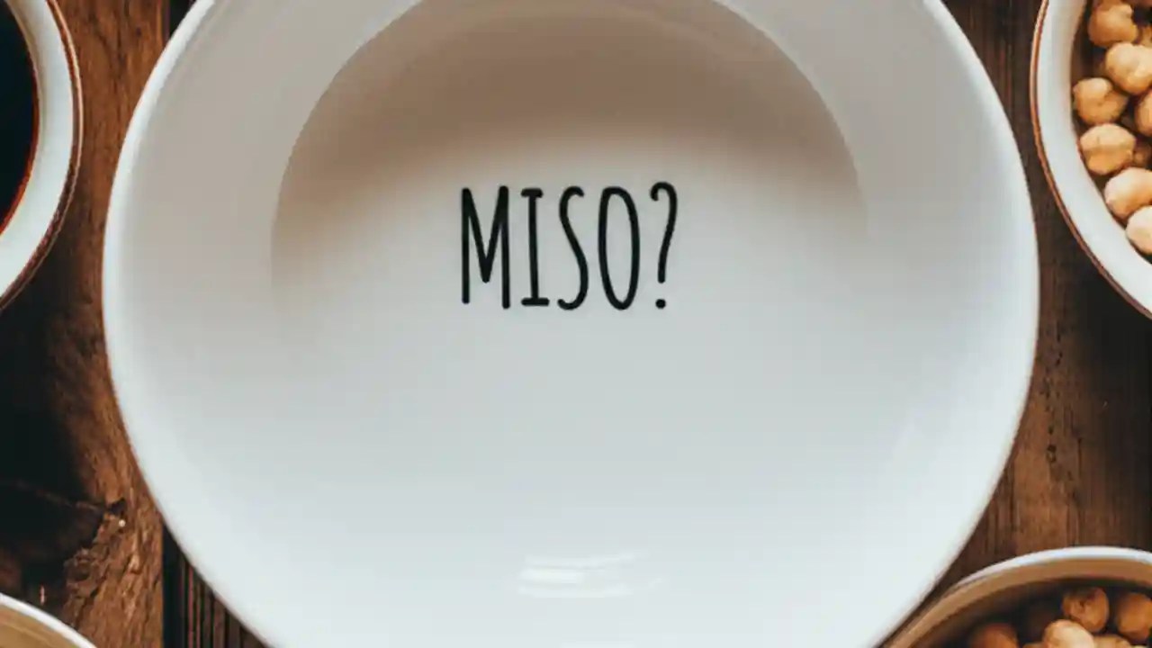 An overhead view of bowls containing miso substitutes like soy sauce, tahini, and nutritional yeast, arranged around an empty bowl labeled MISO.