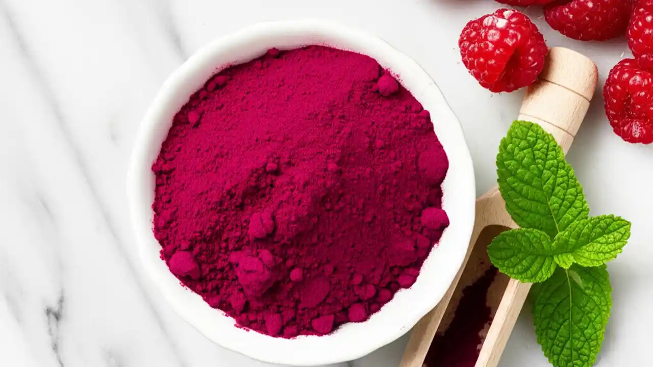 A wooden spoon filled with deep red beetroot powder, next to a sliced raw beet, illustrating the correct daily dosage for health benefits.