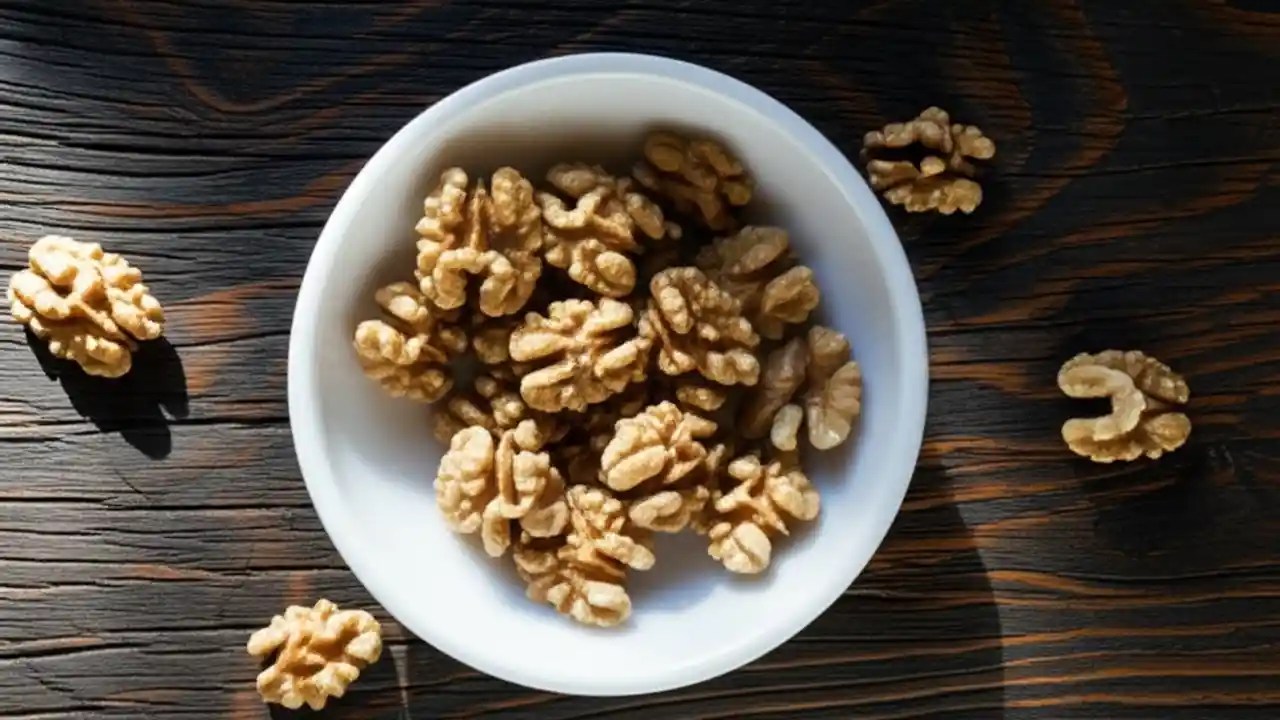 A top-down view of a small wooden bowl containing the recommended daily one-ounce serving of walnuts, which is about 7 whole nuts or 14 halves.